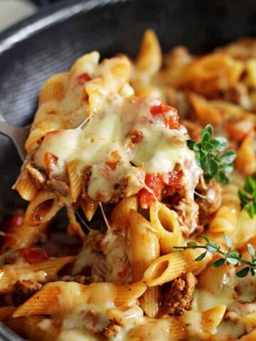 Close up of scoop of cheesy mince pasta with herbs on top