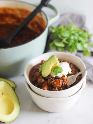 Bowl of chili with avocado, sour cream and pot in background