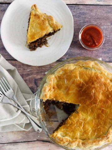 Baked mince and cheese pie with tomato sauce and forks with a slice on a plate