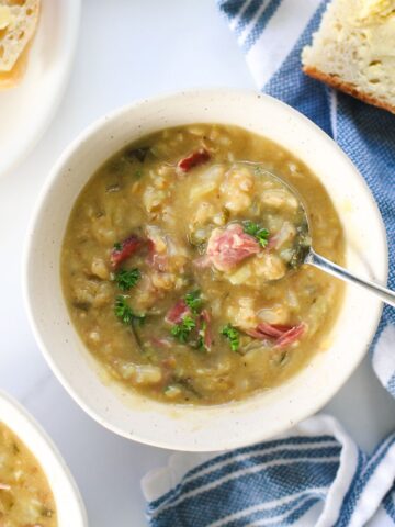 Bowl of bacon bone and vegetable soup on table with slice of buttered bread